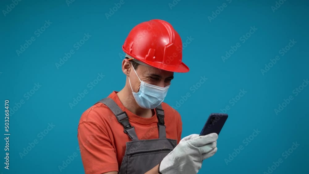 Male builder in face mask browsing social media on smartphone Male builder in face mask browsing social media on smartphone