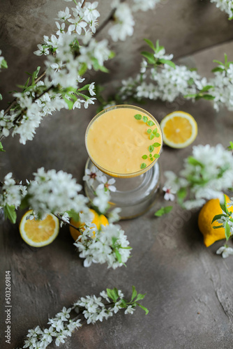Lemon cream in a beautiful glass goblet on a table among lemons and flowering branches.