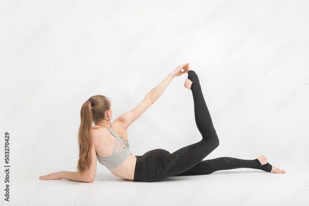 Fitness trainer does flexibility exercise. Gymnast stretches leg. Girl does yoga. Young woman performs asana.