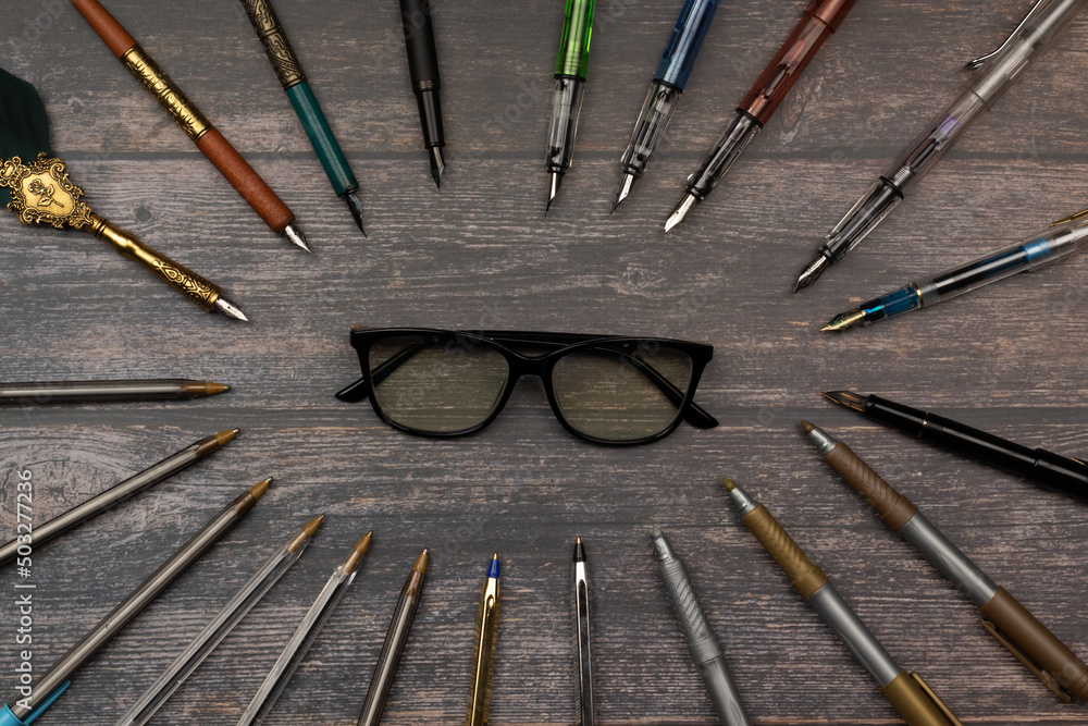 intellectual concept and study. forming an oval of pens, pens, markers surrounding a pair of glasses on a wooden table.