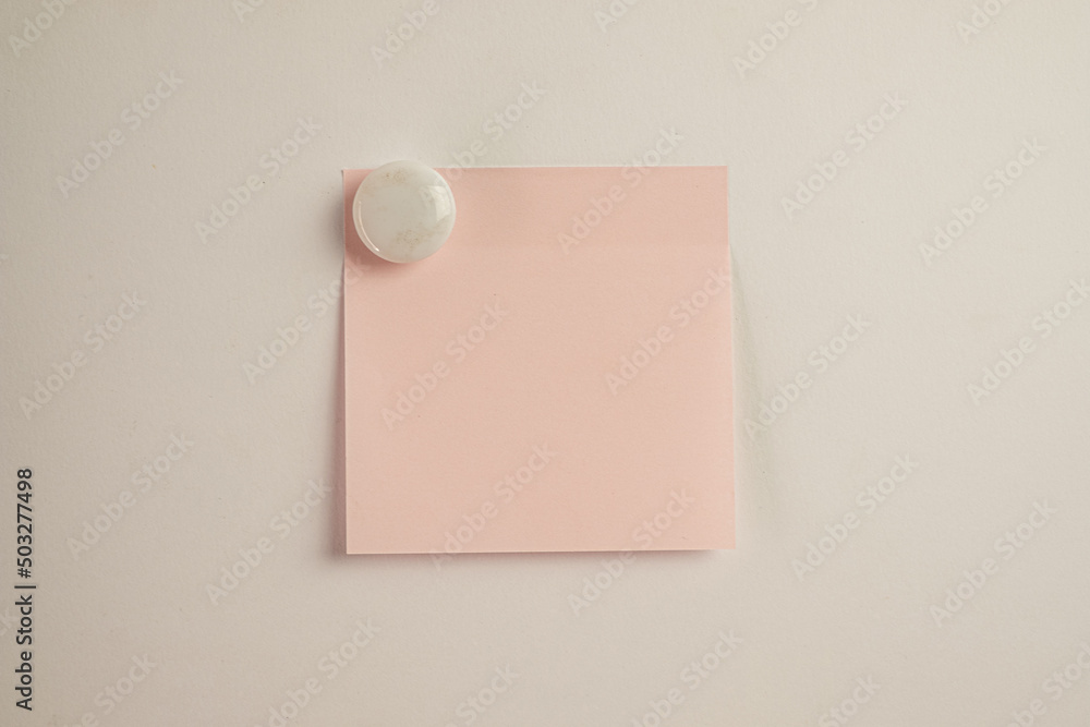 Light Pink sticky note with White circle magnet on white wall background. Light Pink sticky note with White circle magnet on white wall background.