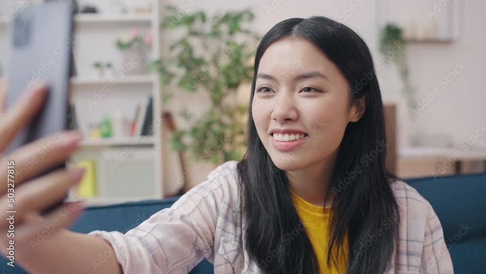 Friendly Asian woman smiling, making video call with friends on smartphone Friendly Asian woman smiling, making video call with friends on smartphone