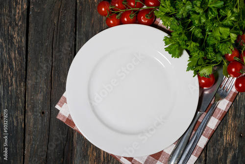 table setting with white plate and vegetables on wooden background