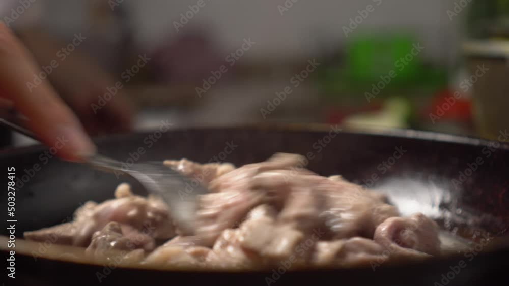 Woman's hand spoons meat in frying pan. She roasts chunks of meat. Close-up. Cast iron. Gas stove in kitchen of housewife. Cooking at home. Background is blurry. Concept of unhealthy diet chalesterol. Woman's hand spoons meat in frying pan. She roasts chunks of meat. Close-up. Cast iron. Gas stove in kitchen of housewife. Cooking at home. Background is blurry. Concept of unhealthy diet chalesterol.