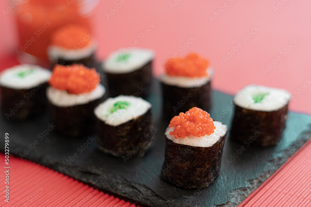 Sushi pieces on a square slate plate, accompanied by red caviar substitute, on a red background. Sushi pieces on a square slate plate, accompanied by red caviar substitute, on a red background.