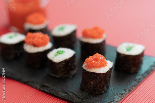 Sushi pieces on a square slate plate, accompanied by red caviar substitute, on a red background.