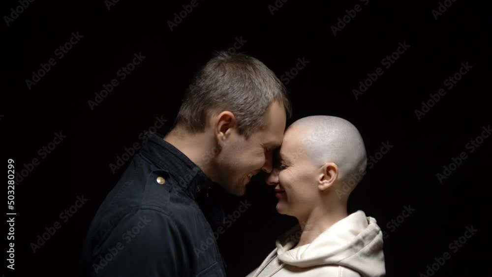 bald woman and her husband hug together against a dark background. copy space bald woman and her husband hug together against a dark background. copy space