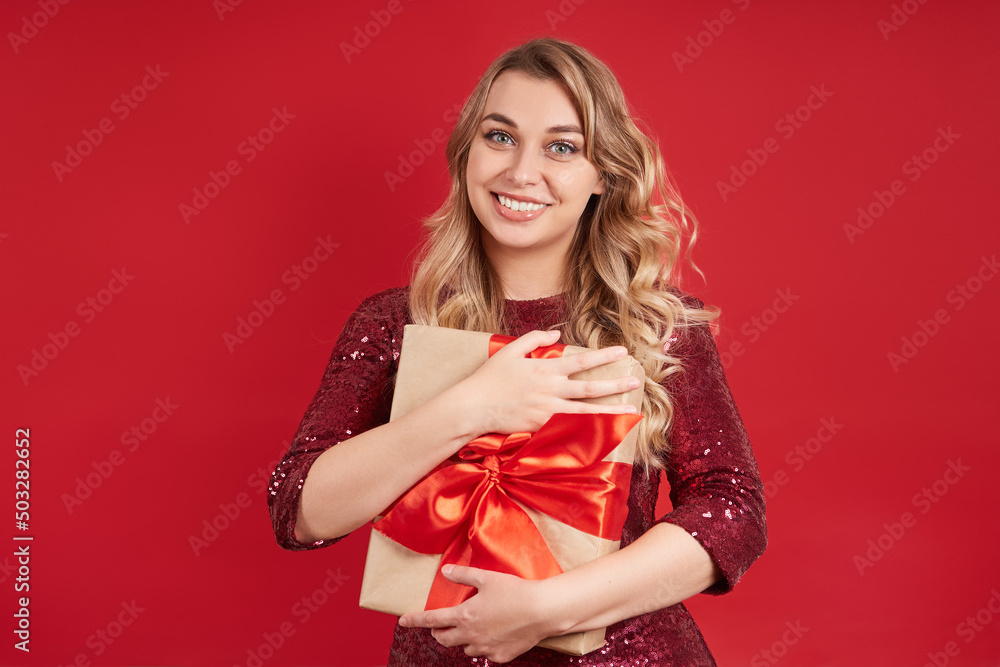 Beautiful cheerful blonde woman holds a gift box in her hands. Isolate on a red background Beautiful cheerful blonde woman holds a gift box in her hands. Isolate on a red background
