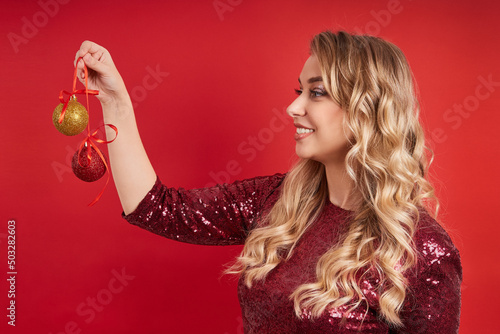 profile portrait of a beautiful young blonde woman with curls in a dress on a red background holds Christmas balls.