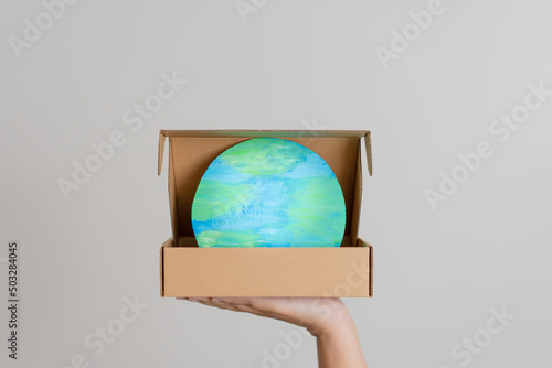 The world in the paper box. Concept of using recycle paper box to save the planet. Woman hand holding cardboard box has crafted world  inside as present or gift for everyone.