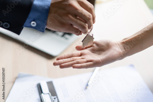close up view hand of property realtor landlord giving key house to buyer tenant.