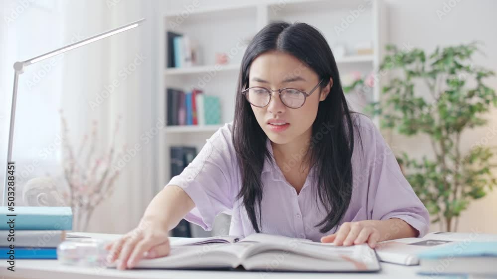 Tired Asian student looking for information in books, feeling academic pressure Tired Asian student looking for information in books, feeling academic pressure