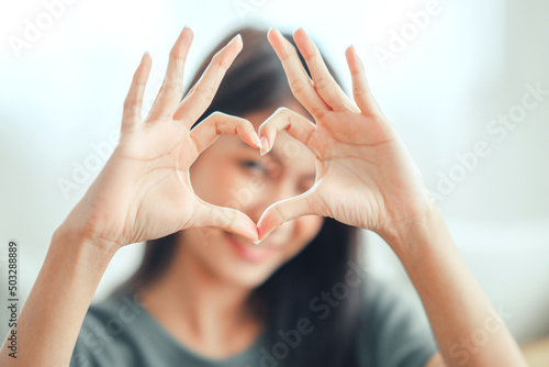 Close up of happy young asian woman smiling and showing hands sign heart shape looking at camera. Healthy heart health life insurance, love and charity, voluntary social work.
