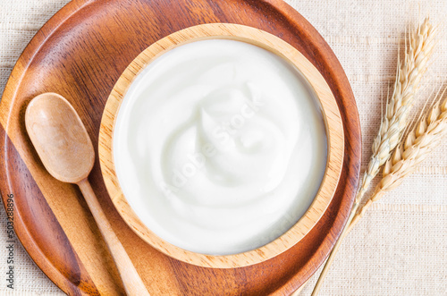 Slika na platnu Greek yogurt in a wooden bowl and dry barley on table.