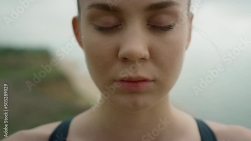 Girl take deep inhale with closed eyes meditating yoga on seashore close up. 