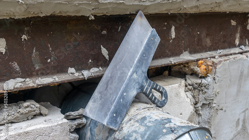 Close-up of a dirty spatula against a wall with plaster. Wall renovation process. Renovation concepts.