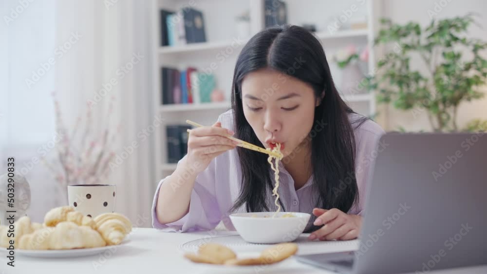 Asian woman eating noodles and watching series on laptop, unhealthy eating habit Asian woman eating noodles and watching series on laptop, unhealthy eating habit
