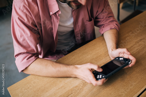 Cropped image of millennial male holding gamepad controller for playing video game indoors, unrecognizable man using joypad switch and 4G internet connection for winning online multi tournament photo