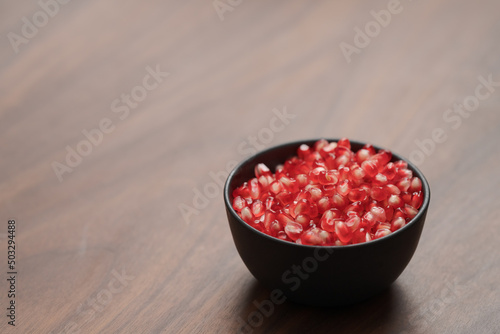 pomegranate seeds in a black bowl on walnut table