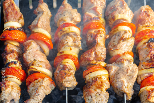 Grilled fried pork meat, pieces of meat on skewers. Process of cooking marinated meat with spices, onions and tomatoes. Outdoor picnic, barbecue. Beef, Veal, Pork, Piglet, Lamb, Mutton, Venison, kebab photo