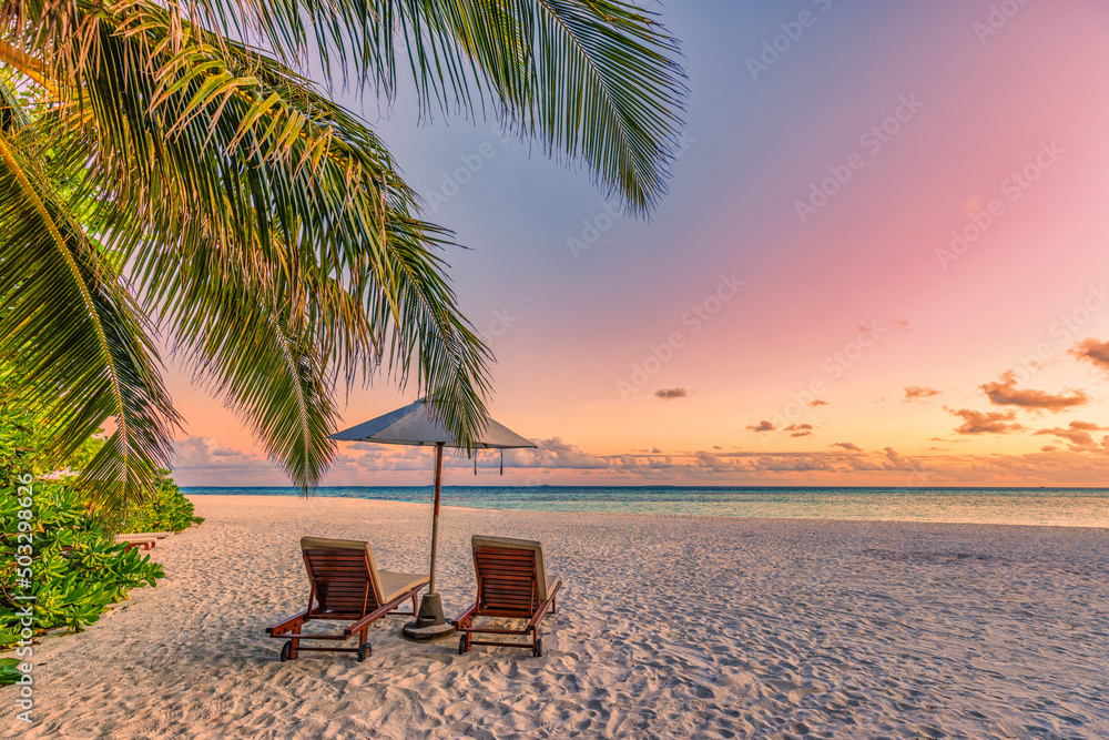 Beautiful tropical sunset landscape, couple sun beds, loungers, umbrella under palm tree. White sand, seaside horizon, colorful twilight sky, calm and relax, recreational. Inspirational beach resort 