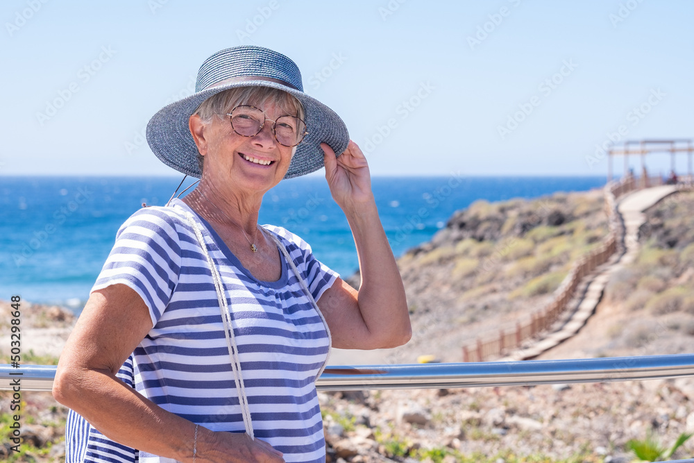 Happiness and good mood in senior smiling woman in outdoors sea excursion. Attractive white haired lady dressed in blue expressing freedom and joy. Horizon over water