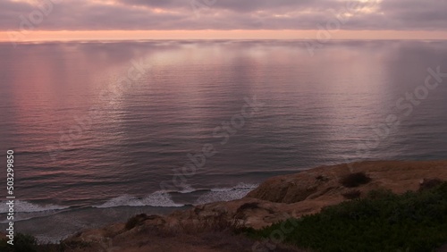 Dramatic cloudscape at sunset  reflection of pink sky  clouds. Torrey Pines scenic vista point  overlook viewpoint  ocean sea water waves from above. Steep cliff  rock or bluff  California coast  USA.