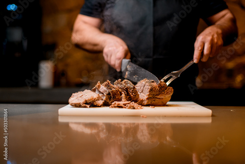Selective focus on delicious fried meat which man cuts to slices on cutting board.
