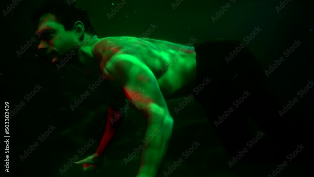 muscular man is swimming underwater, guy is floating in mysterious dark depth of sea or lake muscular man is swimming underwater, guy is floating in mysterious dark depth of sea or lake