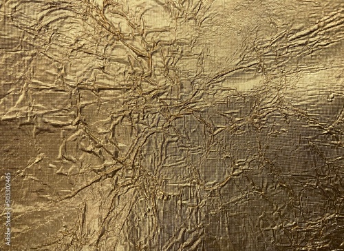 The golden shimmering surface of a metal foil with folds