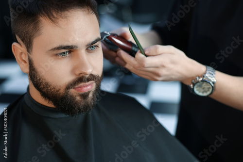 Professional hairdresser working with client in barbershop