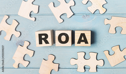 Blank puzzles and wooden cubes with the text ROA Return On Assets lie on a light blue background.