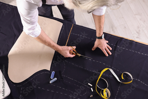 Fototapeta Professional tailor cutting fabric by following chalked sewing pattern at table,
