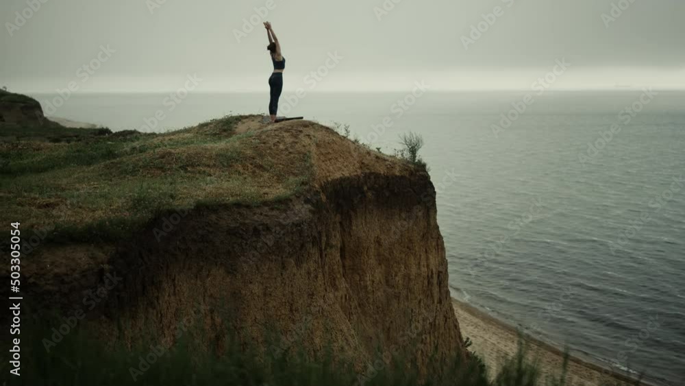 Athletic woman stand straightening up beach hill stretch hands to gray sky. Athletic woman stand straightening up beach hill stretch hands to gray sky.