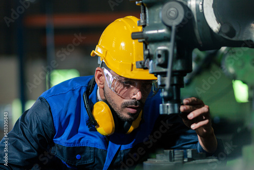 An engineer of mixed-American descent works with industrial machines in a heavy industry. A male worker in a helmet is working on a steel machine. Handsome male engineer working hard