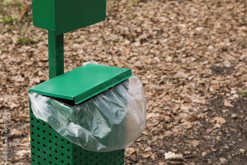 Trash bin with plastic bag in park. Space for text