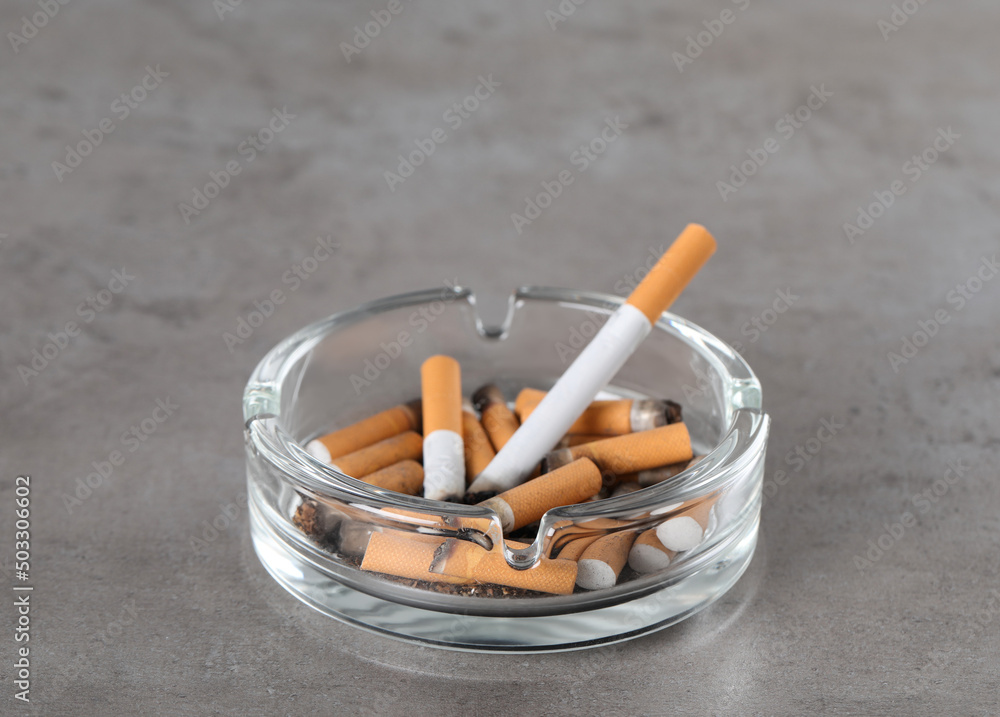 Glass ashtray with cigarette butts on grey table. Space for text Glass ashtray with cigarette butts on grey table. Space for text
