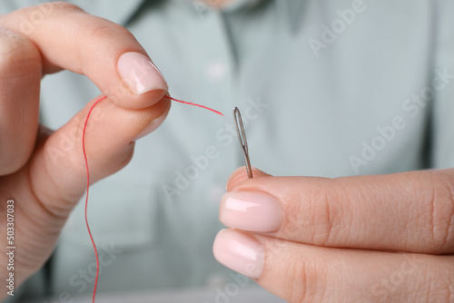 Woman threading needle, closeup view. Sewing equipment