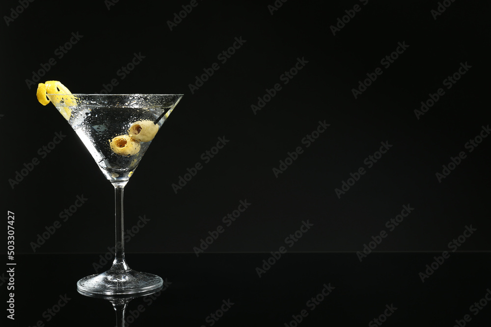 Martini cocktail with olives and lemon twist on dark background, space for text