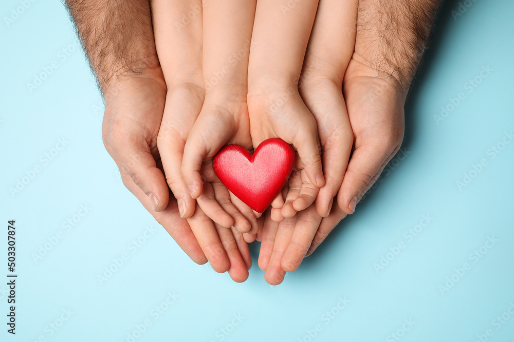 Obraz premium Parents and kid holding red heart in hands on light blue background, top view