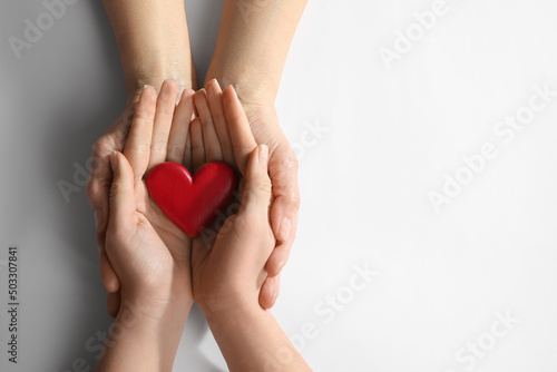 Young and elderly women holding red heart on white background  top view