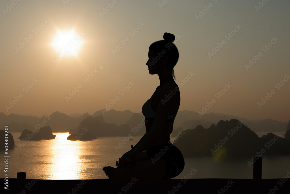 Woman side silhouette in Yoga Easy Meditating pose at sunset with Halong Bay and quiet sea