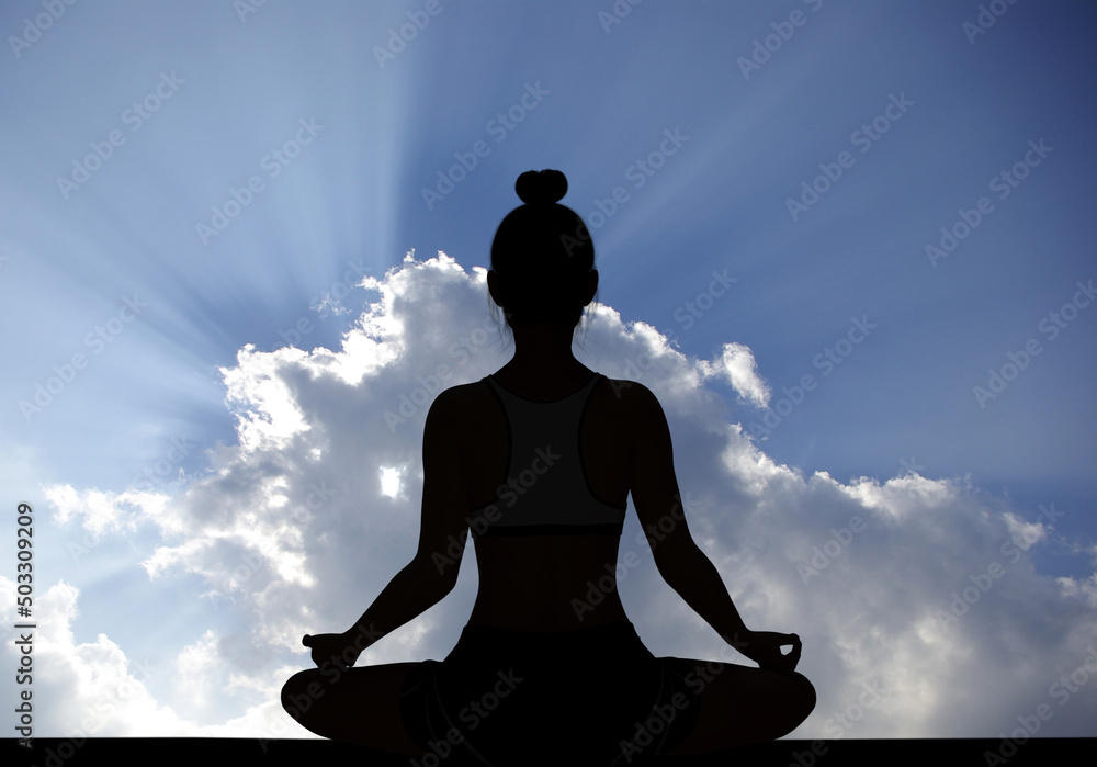 Woman silhouette in Yoga Easy Meditating pose with rays of sunlight through Cloudy sky