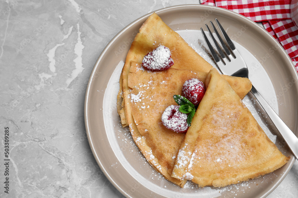 Delicious crepes served with mint, raspberries and powdered sugar on grey table, top view Delicious crepes served with mint, raspberries and powdered sugar on grey table, top view