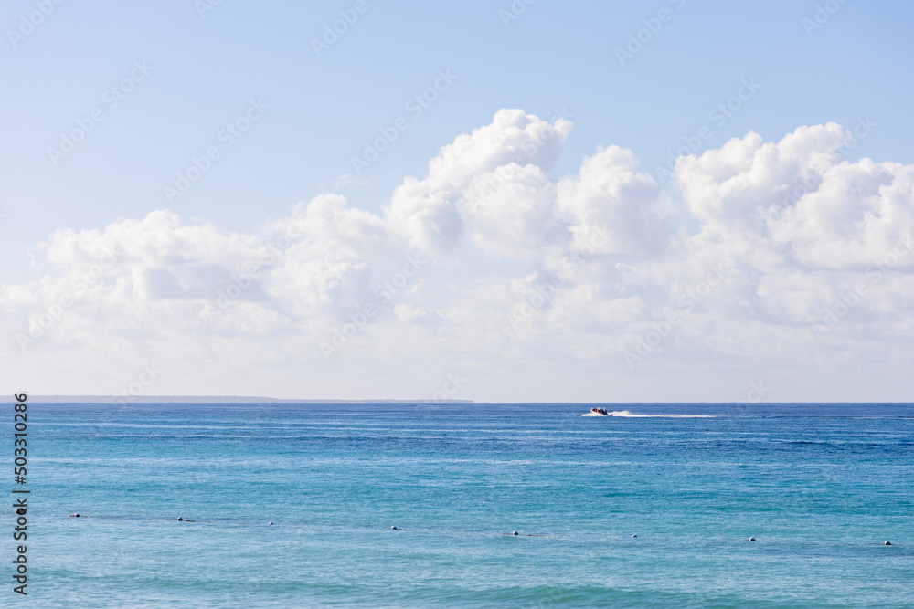 Obraz premium View of the Caribbean Sea in the Dominican Republic,the sea surface,the horizon and a small boat in the distance.Blue sky with clouds and ocean of beautiful color.Beautiful landscapes of the sea coast