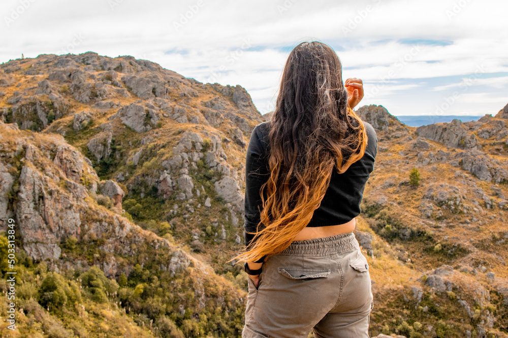 Naklejka premium Portrait of latin woman having fun during trekking day in mountain forest posing on a rock- Back focus