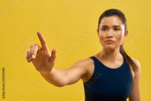 Close up of sporty girl raising hand  holding finger up. Brunette with pony tail looking forward  squint  concentrated  doing yoga. Concept of buddhism and yoga practicing.