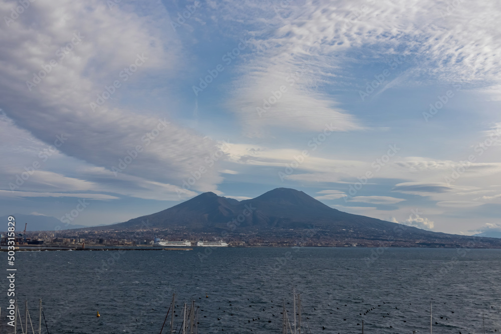 Panoramic view from Castel dell Ovo (Egg Castle) on volcano Mount Vesuvius in Naples, Campania, Italy, Europe. Ferries in the port of Naples. Clouds are accumulating around the mountains. Sea view