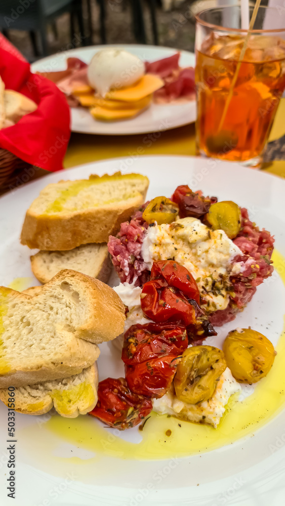 Top view of fresh beef tartare with burrata mozzarella, cocktail tomatoes, toasted white bread and olives. Having a date in the city center in Padua, Veneto, Italy, Europe. Luxury eating Top view of fresh beef tartare with burrata mozzarella, cocktail tomatoes, toasted white bread and olives. Having a date in the city center in Padua, Veneto, Italy, Europe. Luxury eating