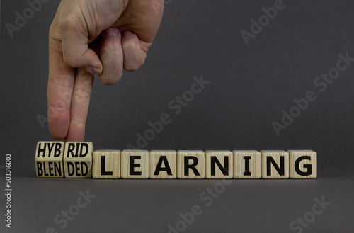 Blended or hybrid learning symbol. Businessman turns cubes, changes words blended learning to hybrid learning. Grey background. Business, education and blended or hybrid learning concept. Copy space.